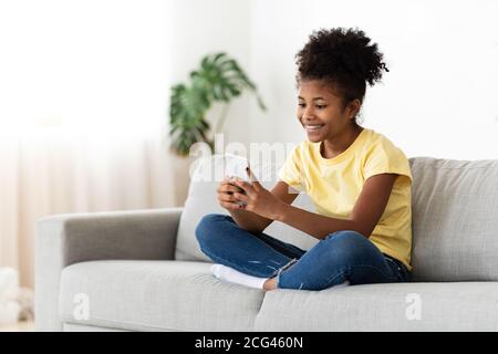 Black Kid Girl jouant en ligne sur un smartphone assis à la maison Banque D'Images