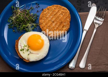 Œuf frit sur du pain grillé et des pousses de cresson vertes fraîches sur une assiette bleue. Vue de dessus. Concept de saine alimentation Banque D'Images