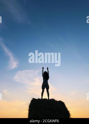 Silhouette de femme debout sur une balle de foin avec ses bras dans l'air, Biélorussie Banque D'Images