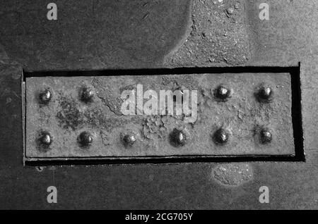 Ancienne plaque rectangulaire rouillée avec rivets sur une surface métallique. Fragment d'un pont métallique avec rivets usés. Arrière-plan multitâche abstrait. Monochrome Banque D'Images