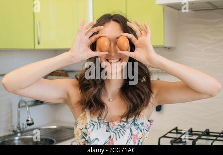 Femme debout dans une cuisine tenant des œufs devant ses yeux Banque D'Images