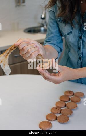 Femme remplissant des macarons au chocolat de ganache au chocolat Banque D'Images