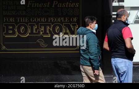 Bolton, Lancashire, 9 septembre 2020. Les habitants de Bolton sont confrontés aujourd'hui à leur première journée complète d'un nouveau verrouillage plus strict. Les pubs, les bars et les restaurants ne sont autorisés qu'à servir un service à emporter, alors qu'il n'est pas permis de rencontrer quelqu'un de l'extérieur de votre famille. Deux hommes dans des masques protecteurs marchent devant un panneau sur les fabricants de pasties locaux magasin de Carrs. Crédit: Paul Heyes/ Alamy Live News Banque D'Images
