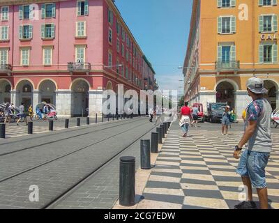 Personnes prenant des photos et marchant près de bâtiments ocre rouges avec ligne de tramway entre eux à la place Massena dans le centre de Nice, France. Banque D'Images