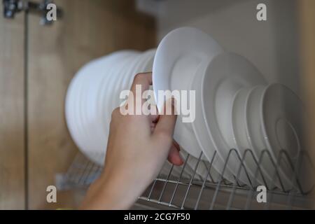 La main de la femme tire les plats blancs propres hors de l'armoire de cuisine. Banque D'Images