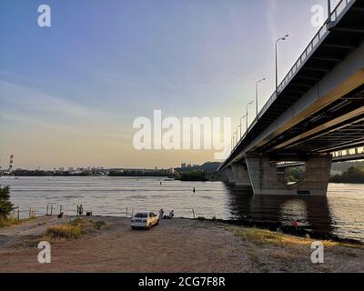 Vue depuis la rive gauche du fleuve Dniepr sur le pont Darnytskyi et la rive droite de la ville de Kiev. Personnes pêchant au coucher du soleil. Banque D'Images