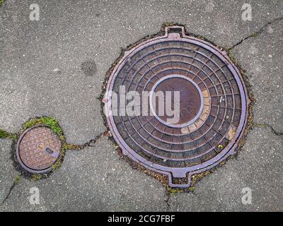 Vue de dessus des deux couvercles de trous d'homme de cercle. Couvercles de vidange en acier dans un asphalte fissuré. Banque D'Images