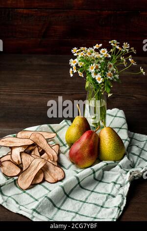 Composition de la vie encore des chamomiles dans vase et frais et poires séchées placées sur une serviette de cuisine Banque D'Images