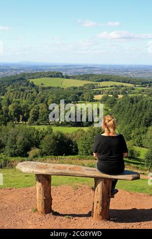 Femme assise sur un banc en profitant de la vue depuis les collines de Cent, Worcestershire, Angleterre, Royaume-Uni. Banque D'Images