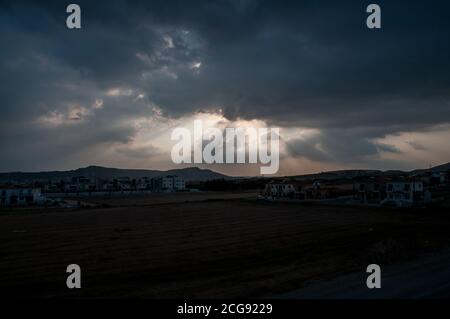 Les rayons du soleil se brisent à travers de lourds nuages au-dessus du paysage silhoueté du sud-est de Chypre. Banque D'Images