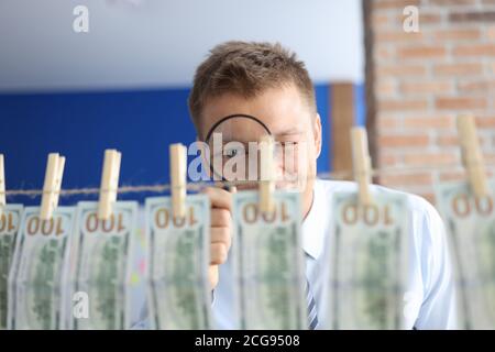 L'homme regarde à travers la loupe à cent billets de dollars accrochés sur des cloespins. Banque D'Images