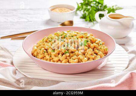 mac vegan et fromage à la sauce levure nutritionnelle dans un bol rose sur une table en bois blanc avec des couverts dorés, vue sur le paysage depuis le dessus, gros plan Banque D'Images