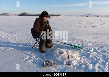 Femme - pêcheur capture du poisson du trou sur un grand lac gelé sur le fond de l'île. Banque D'Images