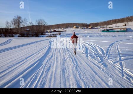 Une fille court le long d'une route d'hiver sur un lac gelé vers un village sur une colline, par une journée ensoleillée d'hiver. Banque D'Images