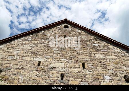 Un mur arrière d'une ancienne maison en pierres, avec double toit glissant. La photo prise à faible angle avec un ciel légèrement couvert sur l'arrière-plan. Banque D'Images