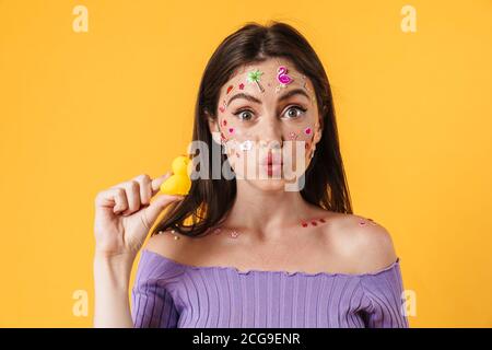 Image d'une jeune femme joyeuse avec autocollants sur la tenue du visage canard en caoutchouc isolé sur fond jaune Banque D'Images