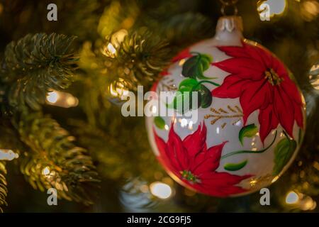 Un ornement avec des fleurs de poinsettia pend du membre d'arbre de Noël Banque D'Images