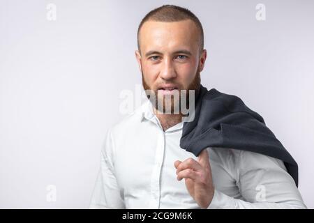 Portrait d'un beau banquier caucasien dans une chemise blanche formelle tenue sa veste élégante sur l'épaule sur fond blanc Banque D'Images