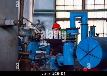 Usine de métallurgie du titane. Jeune métallurgiste près d'un four sous vide. Tube gris et équipement bleu. Banque D'Images