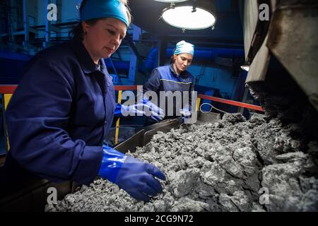 Usine de métallurgie du titane. Deux femmes ouvrières en gants de travail en caoutchouc bleu sélectionnent une éponge en titane pour la production Banque D'Images