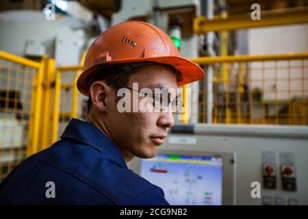 Jeune travailleur asiatique sur une usine de métallurgie du titane. Opérateur de contrôle pour machine à pression pour comprimer l'éponge en titane. Banque D'Images