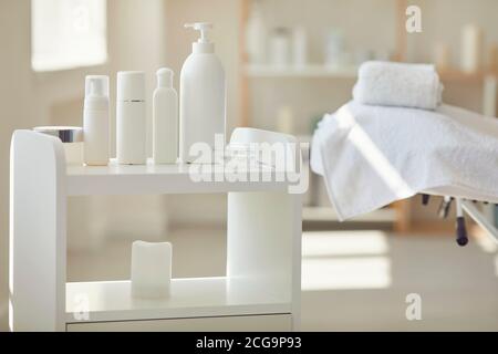 Ensemble de produits de beauté sur une petite table dans la salle de spa avec lit de massage vide en arrière-plan Banque D'Images