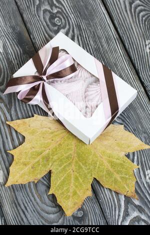Zephyr dans une boîte cadeau. Attaché avec un ruban attaché à un noeud. Feuilles d'érable séchées tout autour. Sur les planches de pin peintes en noir et blanc. Banque D'Images