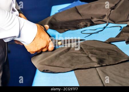Un tailleur, ses mains, travaillant dans son atelier, coupe le tissu sombre avec les ciseaux de l'ancien tailleur, gros plan. Banque D'Images