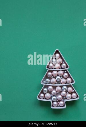 Boules de verre rose pastel dans un bol en forme d'arbre de Noël sur fond vert dans un plan plat avec espace de copie. Célébration de fête ou concept de boulangerie Banque D'Images