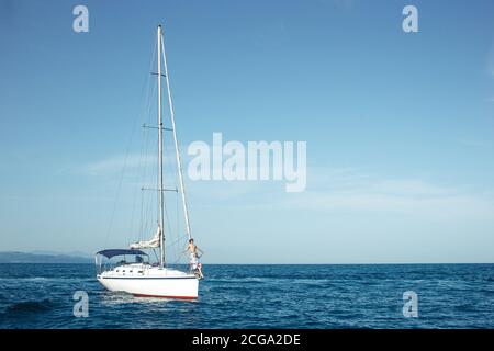 Yacht flottant avec voiles en bas dans la mer calme. Un bateau a abaissé les voiles et ancré près de la côte Banque D'Images