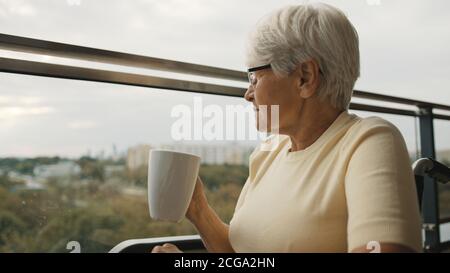 femme âgée en fauteuil roulant sur la terrasse tenant une tasse de thé ou de café. . Photo de haute qualité Banque D'Images