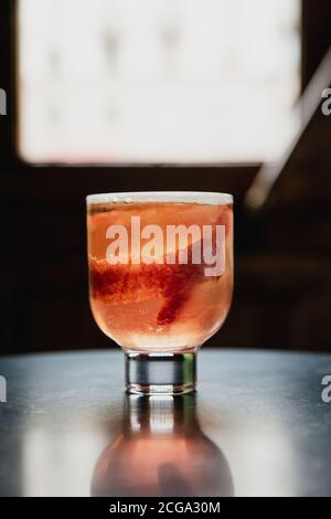 Un beau cocktail rose avec un grand cube de glace dans un verre à boule, garni de sang zeste d'orange, un reflet dans la table en marbre noir Banque D'Images