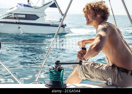 Jeune homme de marin hipster beau avec des poils flous naviguant sur un bateau pour emmener ses amis à un voyage en mer, regardant l'horizon Banque D'Images