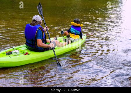 Grand-père et petit-fils assis dans un kayak pour naviguer le long le lac le long des rochers en kayak Banque D'Images