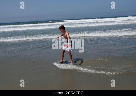 Un adolescent monte sur les vagues les plus proches du rivage de la plage. Banque D'Images