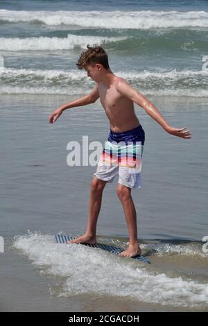 Un adolescent monte sur les vagues les plus proches du rivage de la plage. Banque D'Images