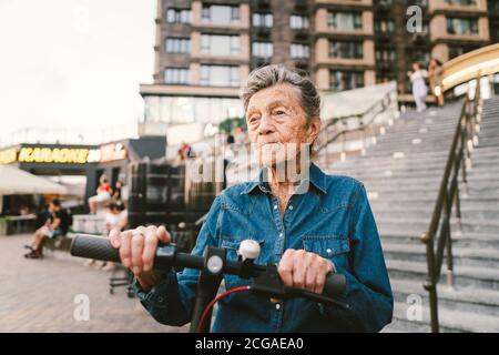 Une vieille femme près du scooter. Grand-mère femme progressiste. Senior s'amuser. La vieille femme apprécie ses passe-temps. Femme à la retraite utilisant un transport moderne et propre Banque D'Images