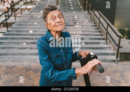 femme de 90 ans avec cheveux gris, rides, progressive et active utilise le scooter électrique moderne de transport. Madame retraité utilise une ville écologique Banque D'Images