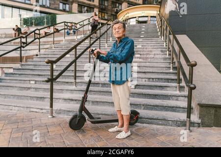 Une vieille femme près du scooter. Grand-mère femme progressiste. Senior s'amuser. La vieille femme apprécie ses passe-temps. Femme à la retraite utilisant un transport moderne et propre Banque D'Images