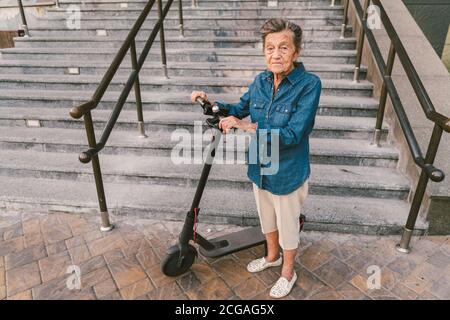 Une vieille femme près du scooter. Grand-mère femme progressiste. Senior s'amuser. La vieille femme apprécie ses passe-temps. Femme à la retraite utilisant un transport moderne et propre Banque D'Images