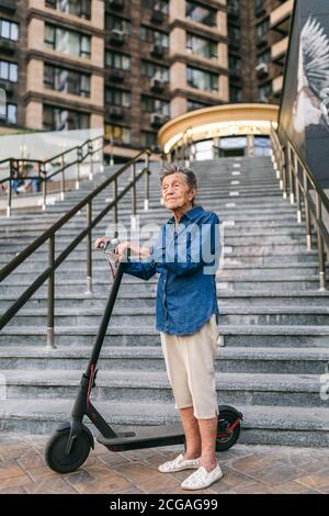 Une vieille femme près du scooter. Grand-mère femme progressiste. Senior s'amuser. La vieille femme apprécie ses passe-temps. Femme à la retraite utilisant un transport moderne et propre Banque D'Images