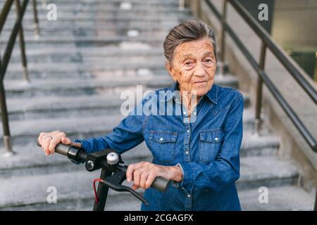 Une vieille femme près du scooter. Grand-mère femme progressiste. Senior s'amuser. La vieille femme apprécie ses passe-temps. Femme à la retraite utilisant un transport moderne et propre Banque D'Images