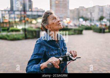 Une vieille femme près du scooter. Grand-mère femme progressiste. Senior s'amuser. La vieille femme apprécie ses passe-temps. Femme à la retraite utilisant un transport moderne et propre Banque D'Images