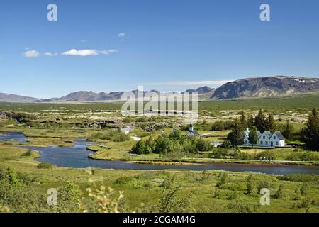 Vue sur la vallée du Rift dans laquelle se trouve le parc national de Thingvellir. Une rivière traverse des champs verts et passe devant l'église Thingvellir. Banque D'Images