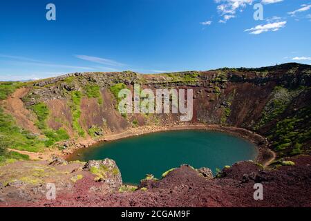 Le cratère de Kerid par une journée ensoleillée au ciel bleu. La roche volcanique rouge est recouverte de mousse vert vif. Partie du cercle d'or en Islande Banque D'Images