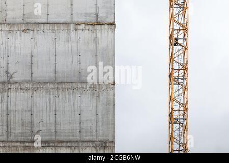 La grue de la tour se fragmente près du mur en béton d'une maison vivante en construction. Bloc de développement d'appartements Banque D'Images