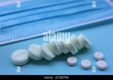 Pile de pilules blanches, et coronavirus médical masque jetable sur fond bleu avec espace de copie. Banque D'Images