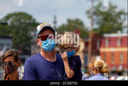 Annapolis, MD, Etats-Unis 08/21/2020: Une famille caucasienne portant des masques pour le visage en raison de COVID-19 marche sur le quai de la ville par une journée ensoleillée. Le père porte sa bl Banque D'Images
