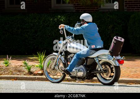Chestertown, MD, USA 08/30/2020: Un homme portant un casque, un Jean et un manteau décontracté est à cheval sur une moto d'époque dans la ville. Il a un sac de selle marron wh Banque D'Images