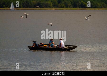 Eastern Neck Island, 08/30/2020: Trois personnes se détendent sur un petit bateau de pêche en bois. L'un dort, les deux autres parlent. Un troupeau d'eau Banque D'Images